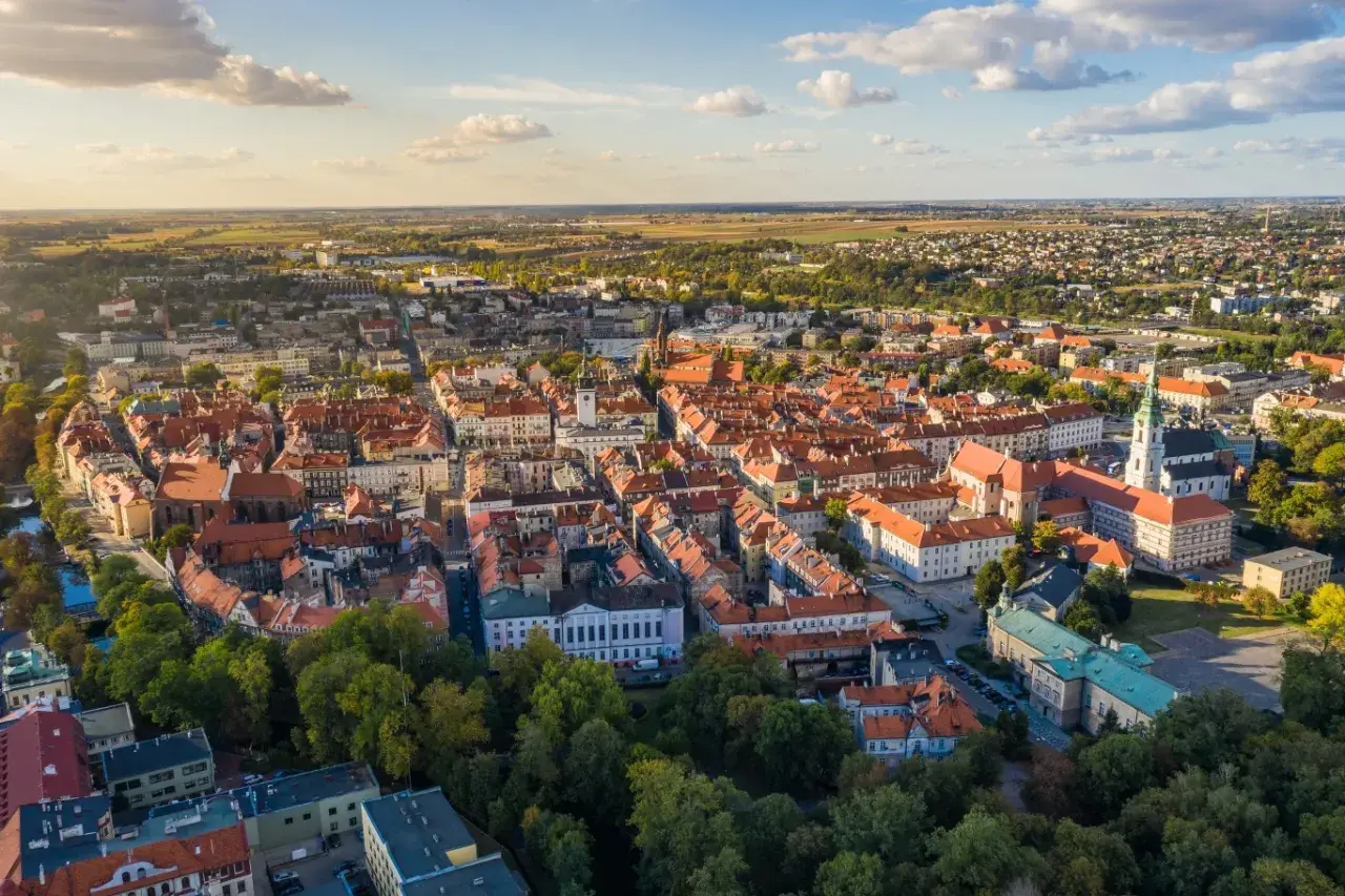 Widok z lotu ptaka na zabytkowe centrum Kalisza, najstarszego miasta w Polsce, z charakterystyczną czerwoną dachówką i zielenią drzew.