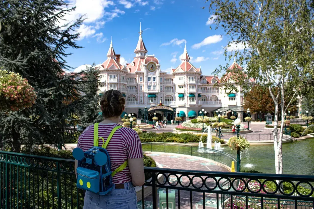 Dziewczyna z plecakiem w kształcie Myszki Miki patrzy na zamek w Disneylandzie. Zastanawia się, ile kosztuje bilet do Disneylandu.