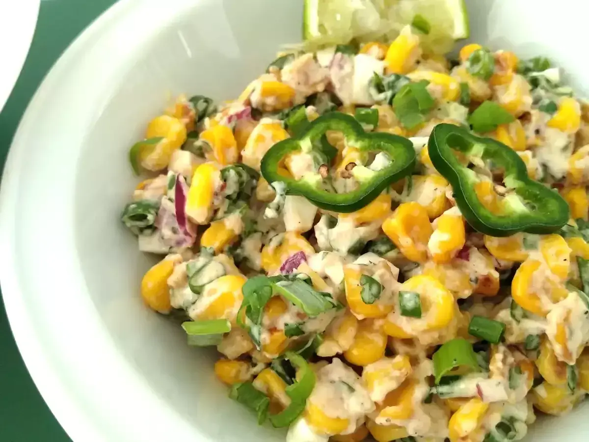 Deliciosa ensalada de maiz cremosa con jalapeños, cebolla morada y cebollín, servida en un tazón blanco.