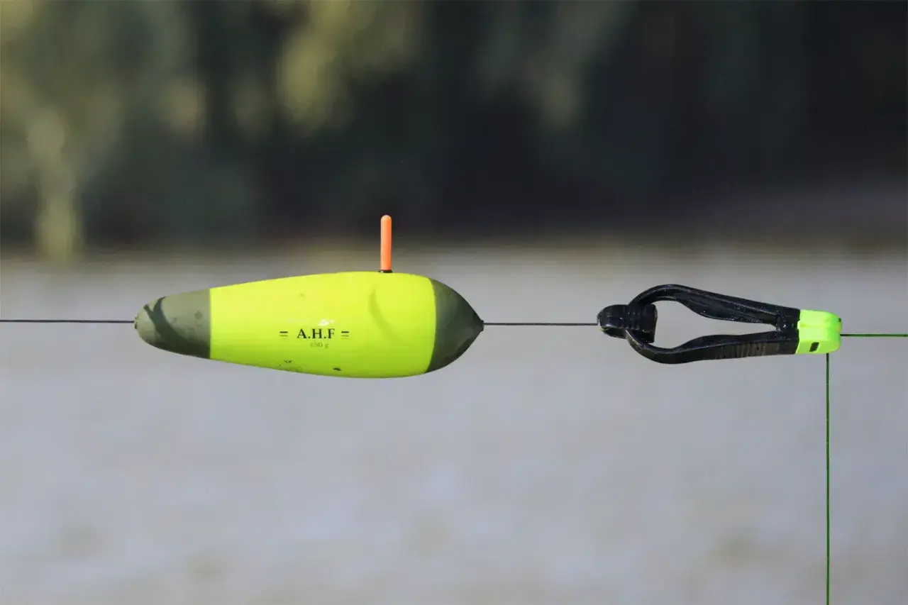 Gelber Wels-Schwimmer mit orangefarbenem Antennenstift und schwarzem Clip an einer Angelschnur.