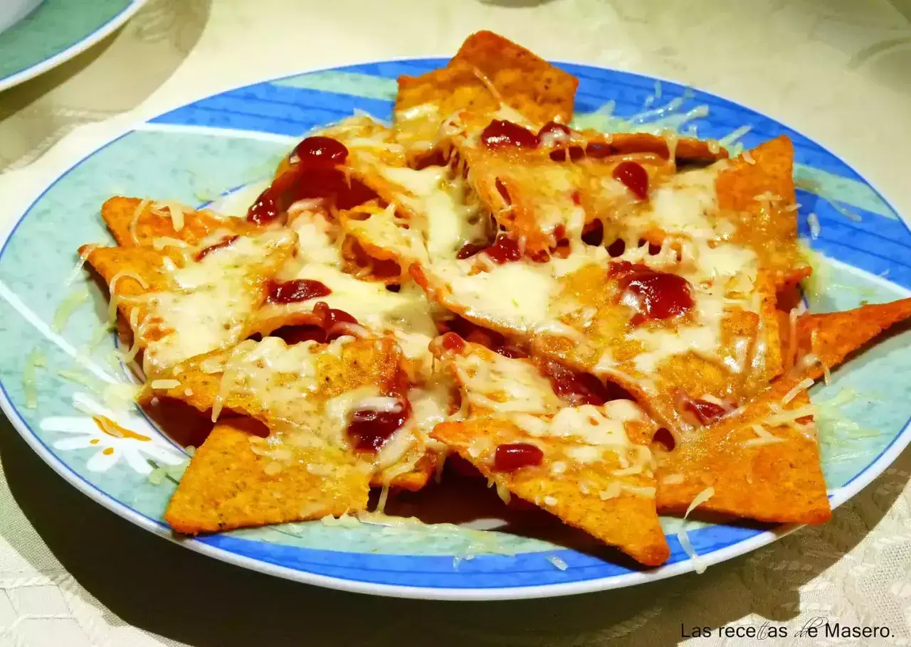 Nachos con queso derretido y salsa roja, servidos en un plato azul y verde. ¡Un antojo irresistible!