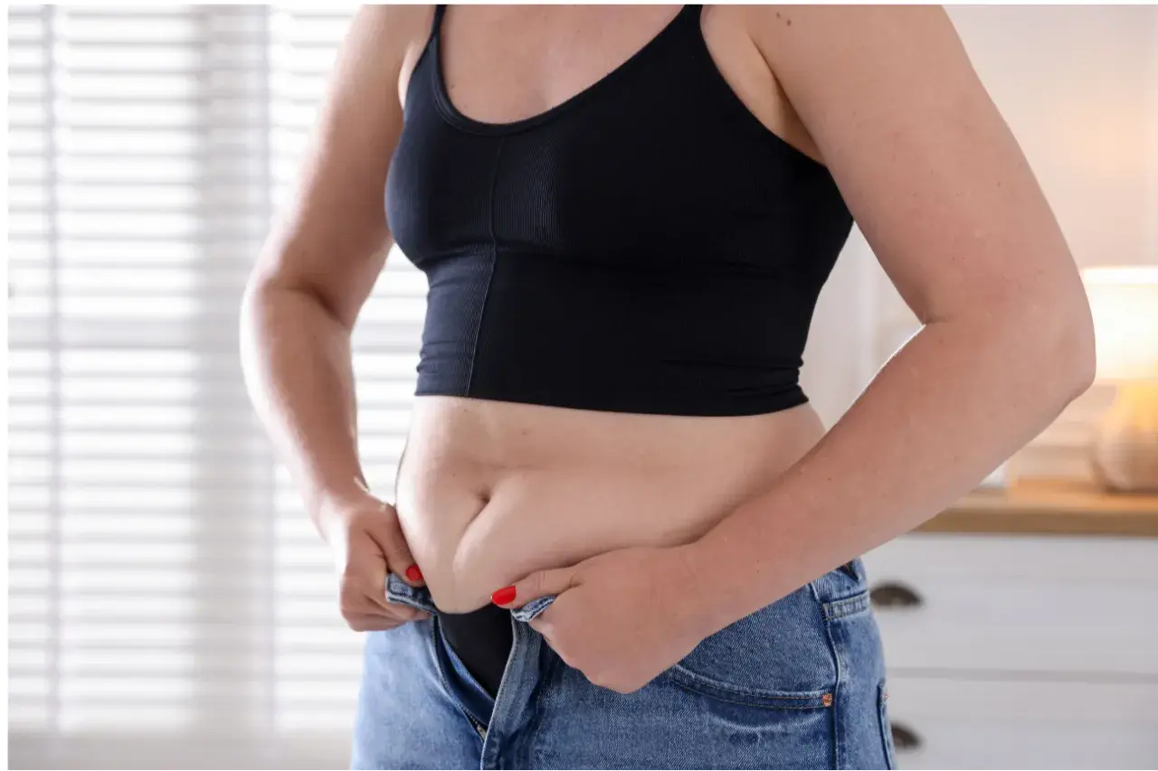 Frau kämpft mit dem Hosenknopf, um den hormonbauch loszuwerden.