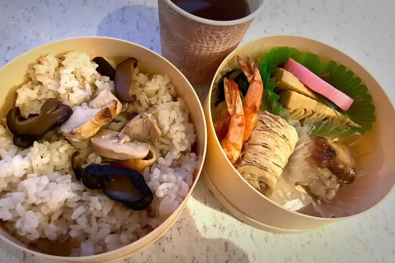 A delicious ekiben, meaning train bento, with rice, chicken, mushrooms, shrimp, and other treats, perfect for a journey.
