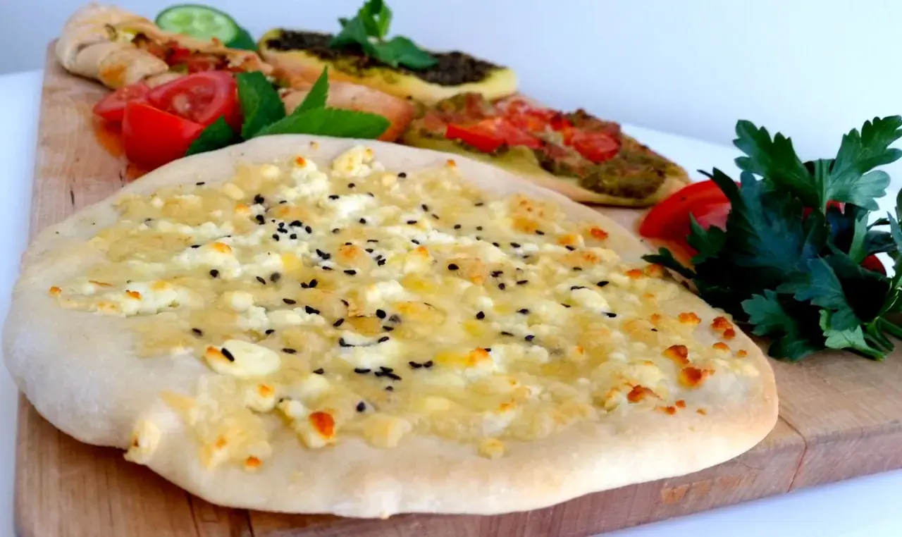 Manakish recept: Färsk ost och svarta sesamfrön på en tunn botten, med andra varianter i bakgrunden.