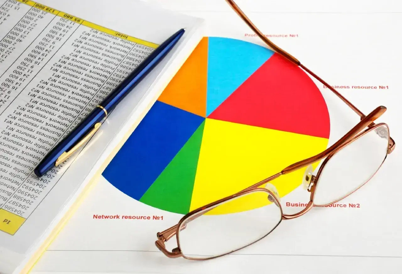 Okulary, długopis i kolorowy wykres kołowy na tle dokumentów z danymi. Analiza danych i rmua.