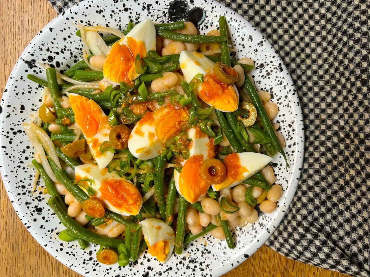 Ensalada de judías verdes, huevos duros, alubias blancas y aceitunas, aderezada con cebolleta picada.