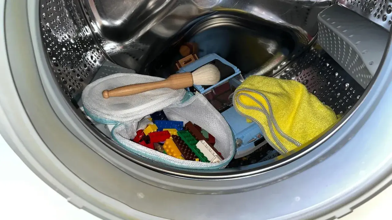 Bunte Duplo-Steine in einem Wäschenetz, ein Spielzeugauto, eine Bürste und ein gelbes Tuch warten auf die Reinigung in der Waschmaschine.