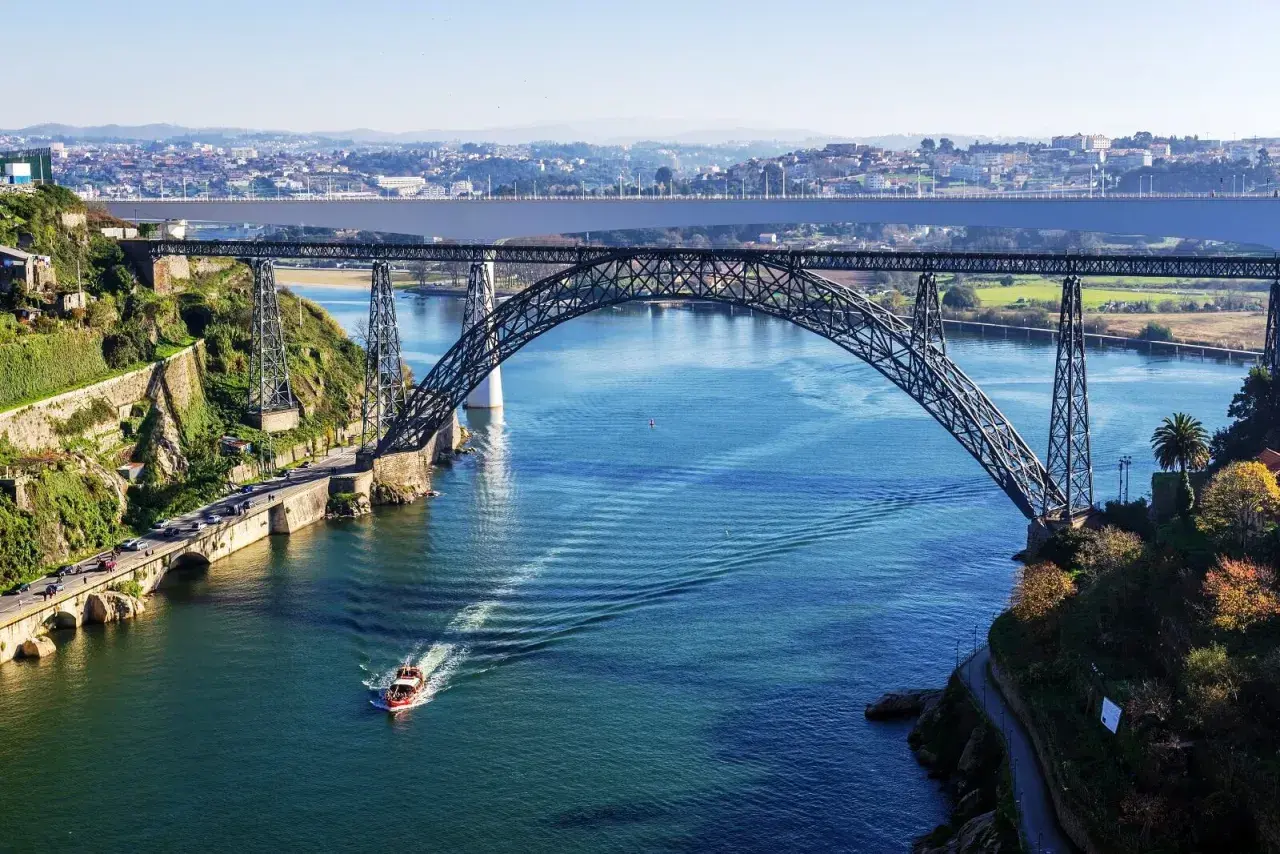 Majestatyczny porto most nad błękitną rzeką, z łodzią przecinającą fale i miastem w tle.