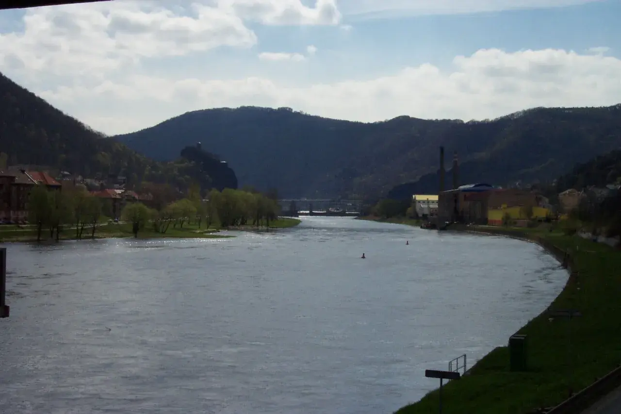 Flusslandschaft bei Ústí nad Labem mit bewaldeten Hügeln, Industriegebäuden und einer Stadt am Ufer.