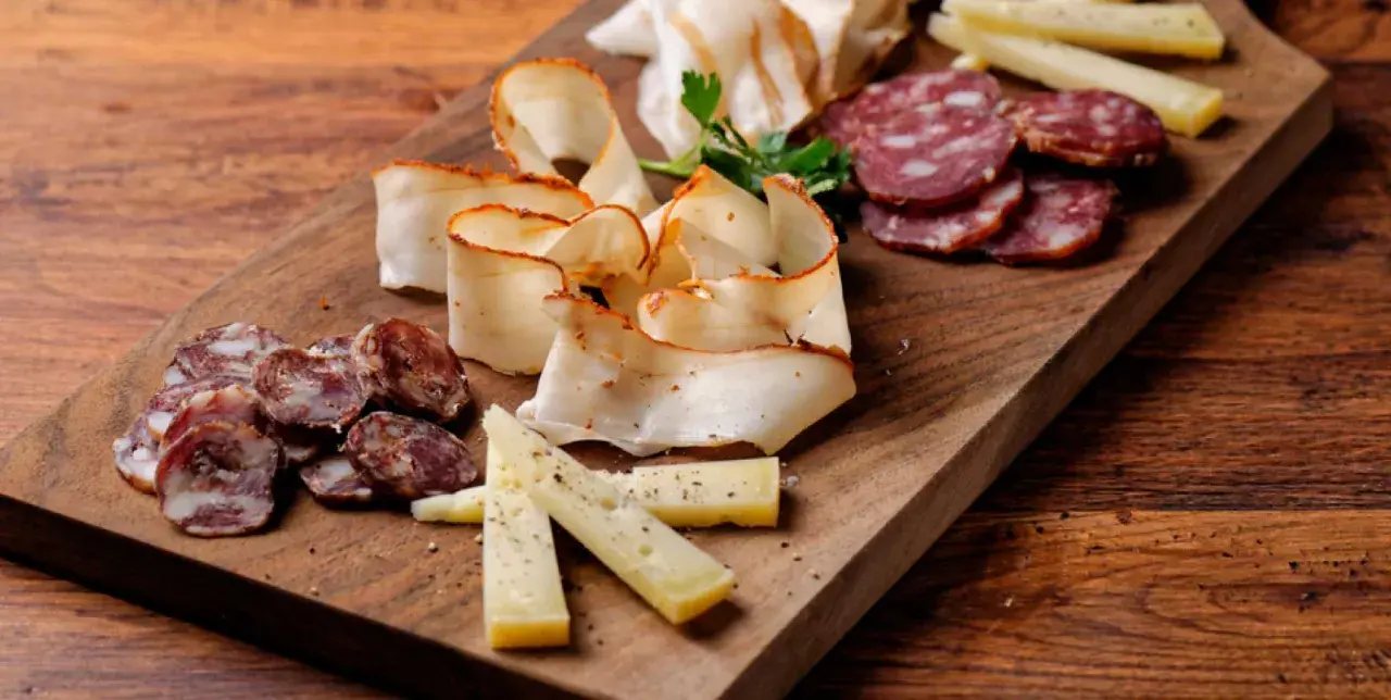 Un invitante tagliere di antipasti con salumi affettati, formaggio e lardo su un tagliere di legno rustico.
