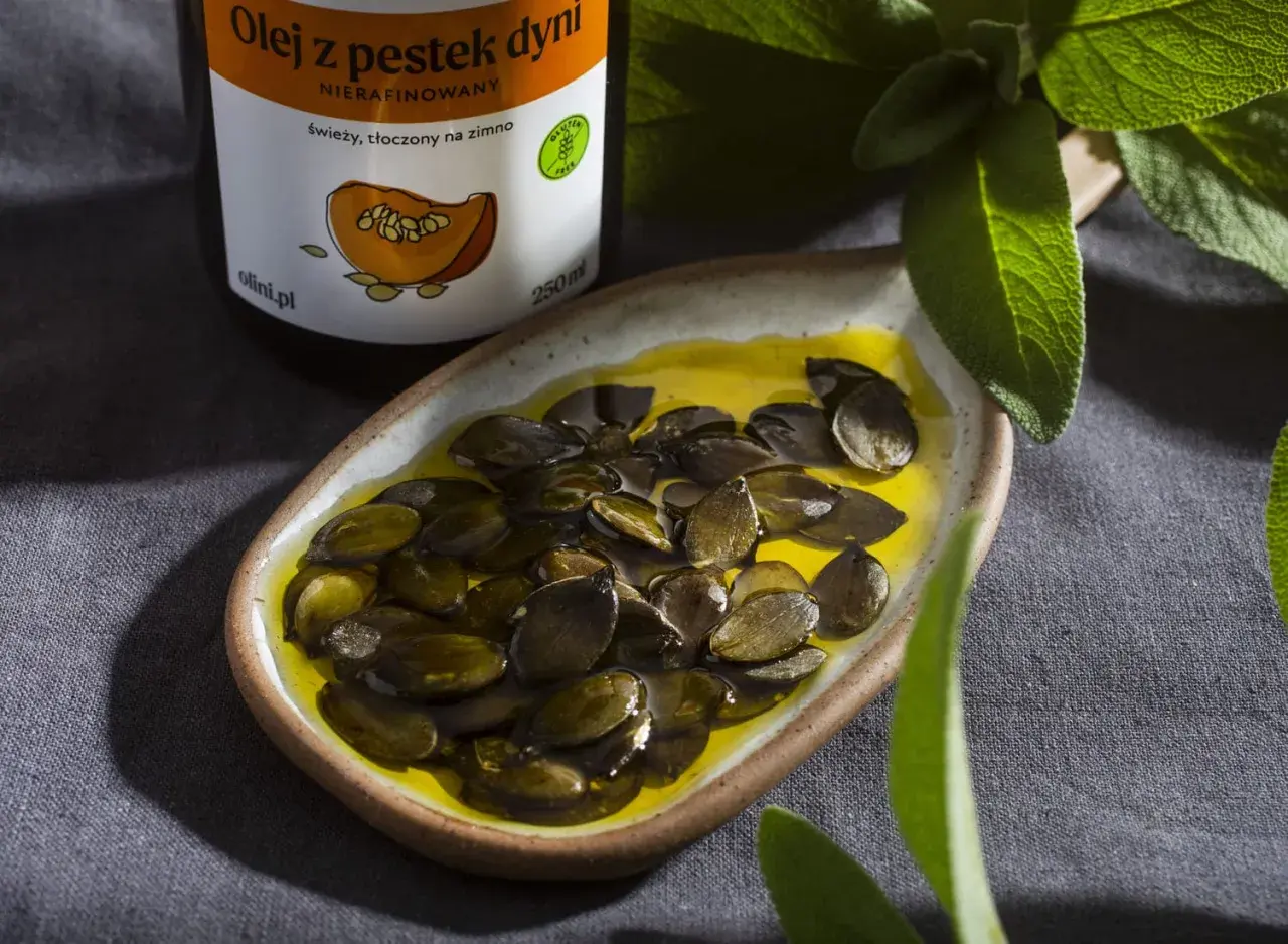 Olej z pestek dyni, świeży, tłoczony na zimno, w miseczce z pestkami i zielonymi liśćmi. Odkryj jego właściwości!
