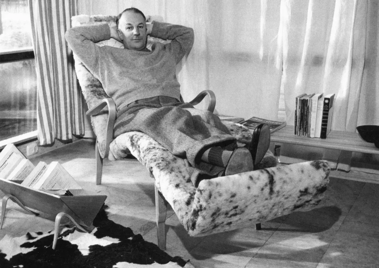 Man vilar i en Bruno Mathsson liggfåtölj, klädd i fårskinn. Böcker och tidningar ligger utspridda.
