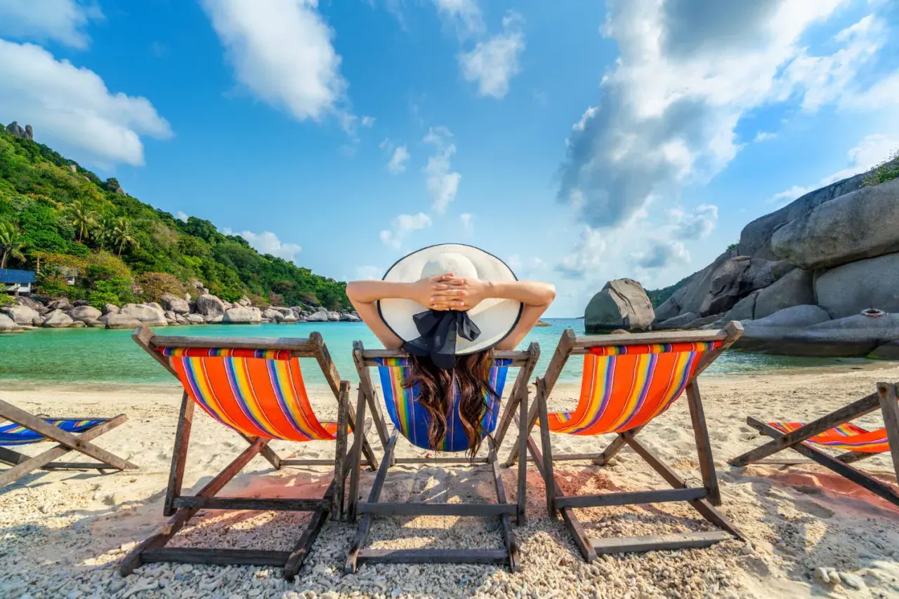 Kobieta w kapeluszu odpoczywa na leżaku na tropikalnej plaży.