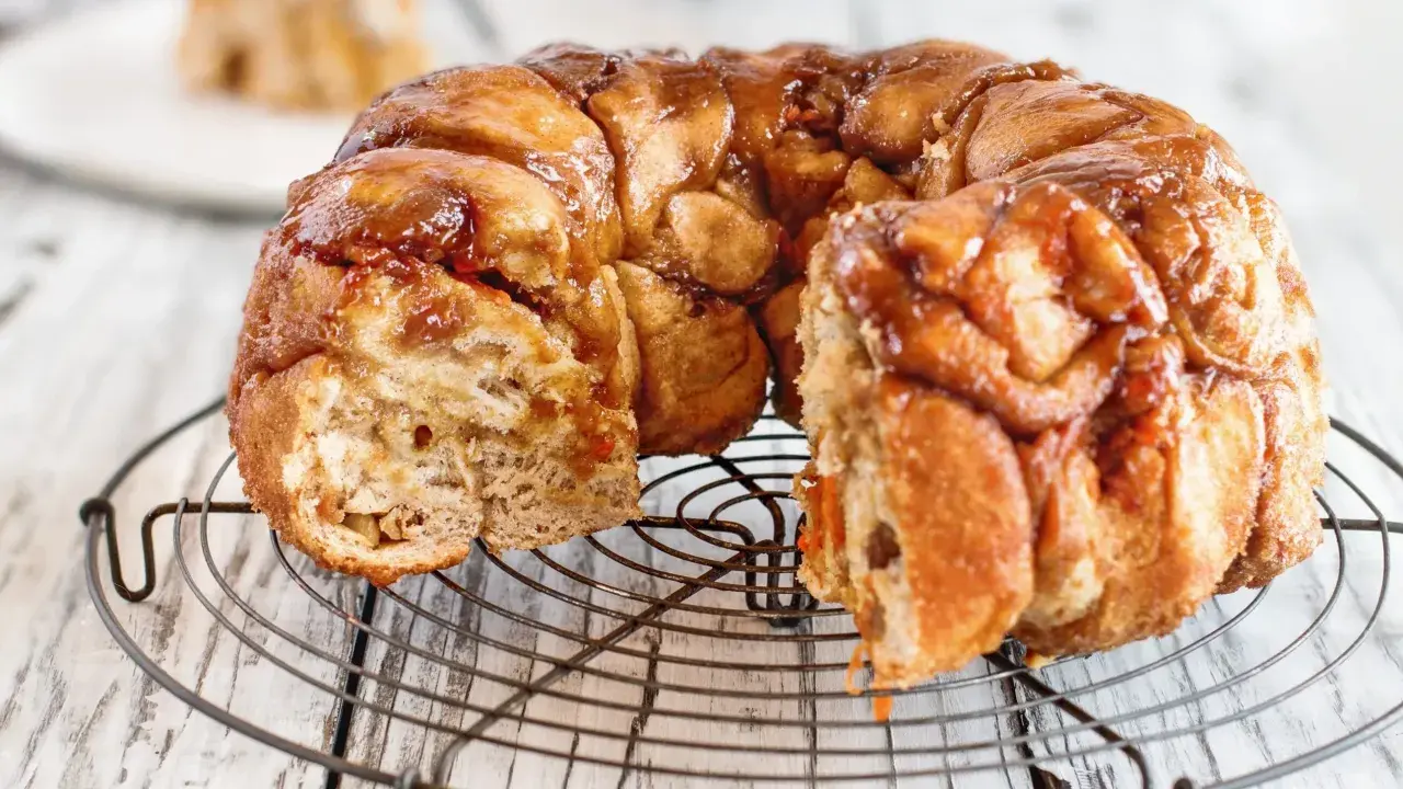 Pyszny, karmelizowany monkey bread przepis na okrągłej kratce. Ciasto jest lekko rozwarstwione, z widocznymi kawałkami ciasta.