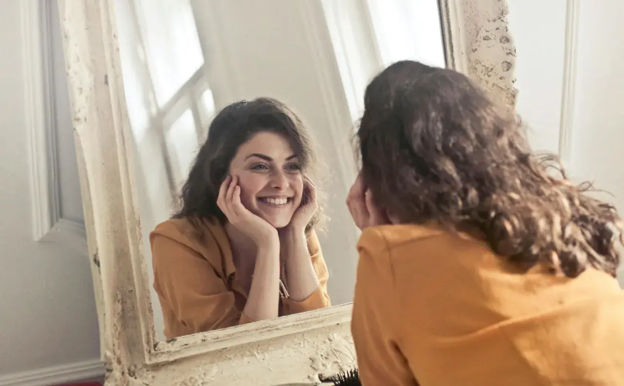 Donna sorride guardandosi allo specchio, un momento di riflessione sull'effetto specchio psicologia e sull'accettazione di sé.
