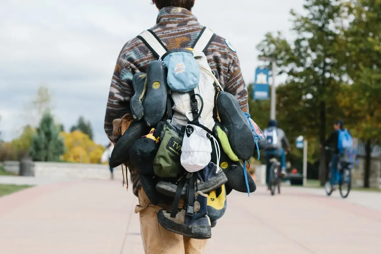 A climber's backpack is laden with multiple pairs of climbing shoes, a testament to a day of ascents.