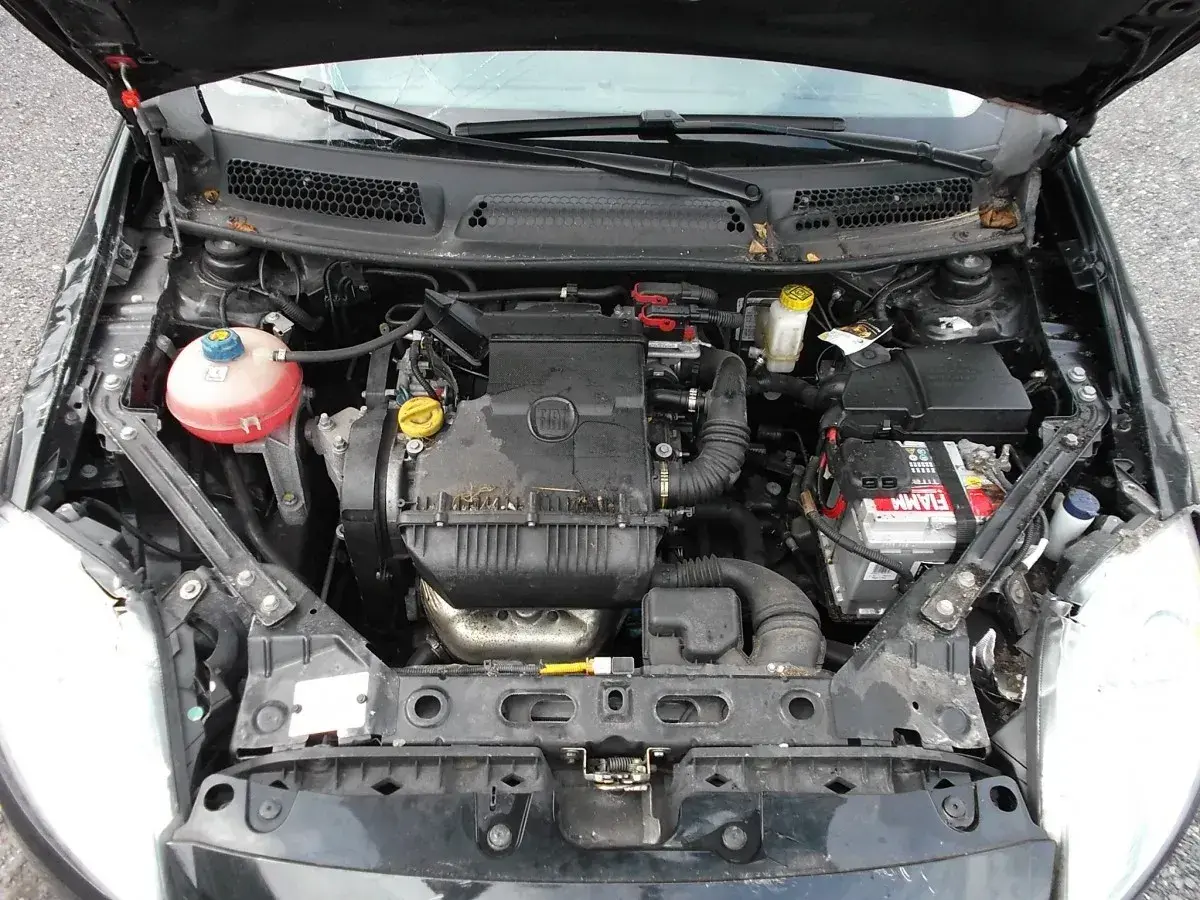 Silnik w fiat bravo 2011, widok z góry. Widać akumulator, zbiornik płynu chłodniczego i elementy silnika.