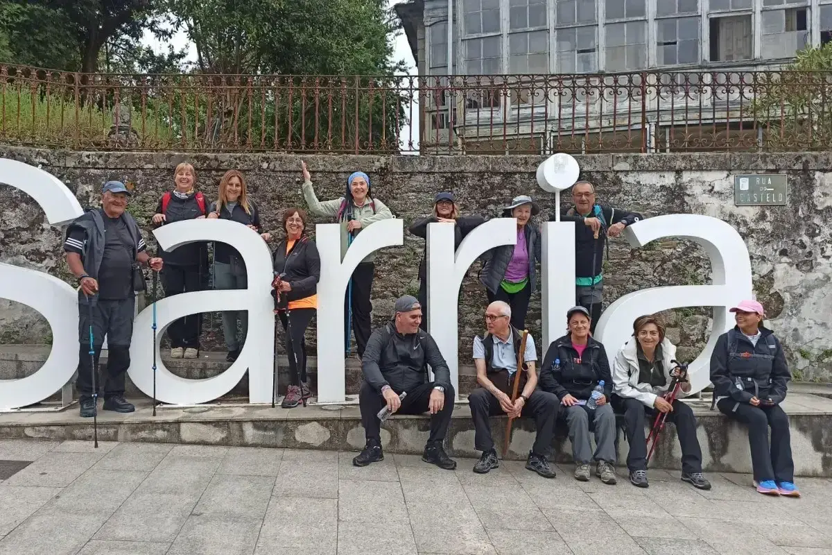 Grupo de peregrinos posa frente a las letras gigantes de Sarria, final de su **tren Santiago Sarria**.