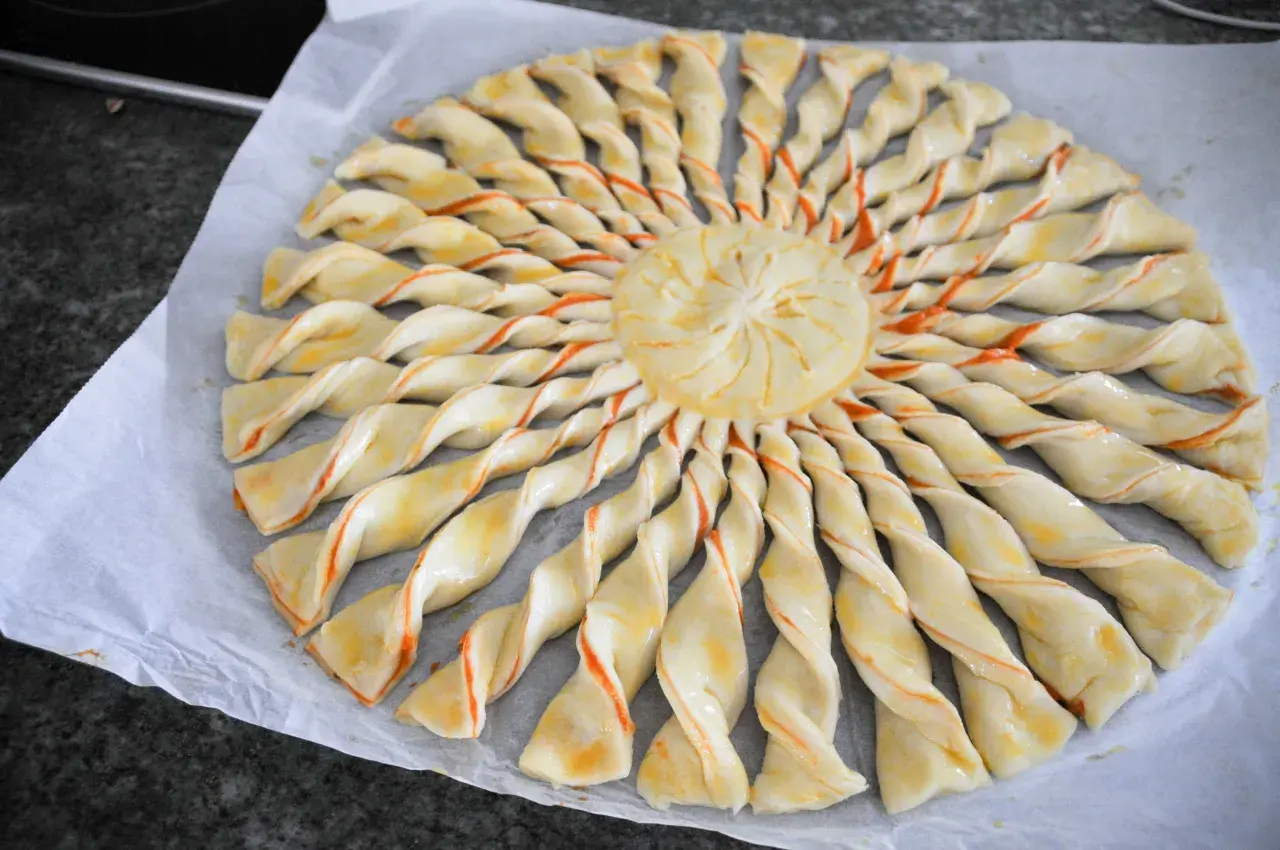Tarte soleil prête à cuire, avec sa pâte feuilletée torsadée et son centre décoré. Un délice visuel et gustatif.