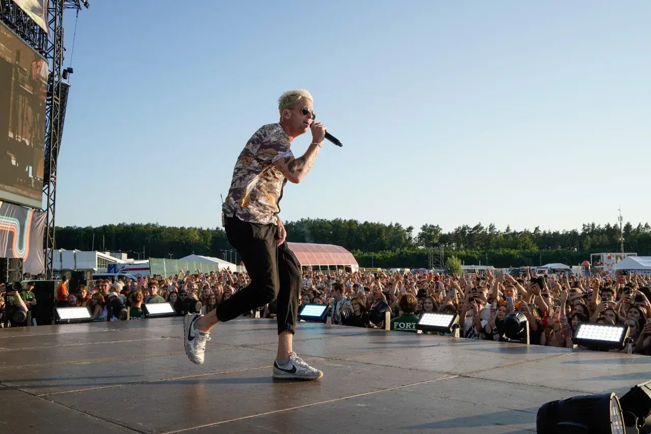 Wokalista One Republic na koncercie, śpiewa do mikrofonu na scenie przed rozentuzjazmowanym tłumem fanów.