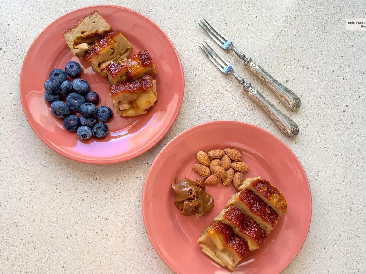 Dos platos rosados con porciones de pudin de manzana, arándanos y almendras. Un postre casero para disfrutar.