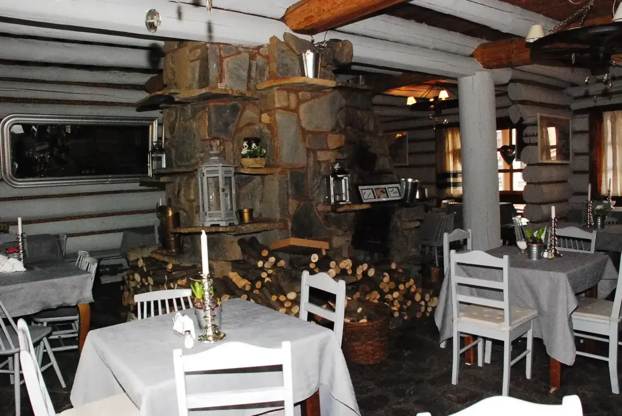 Przytulne bistro prosto z targu, z kamiennym kominkiem i drewnianymi belkami. Stoły nakryte szarymi obrusami, białe krzesła.