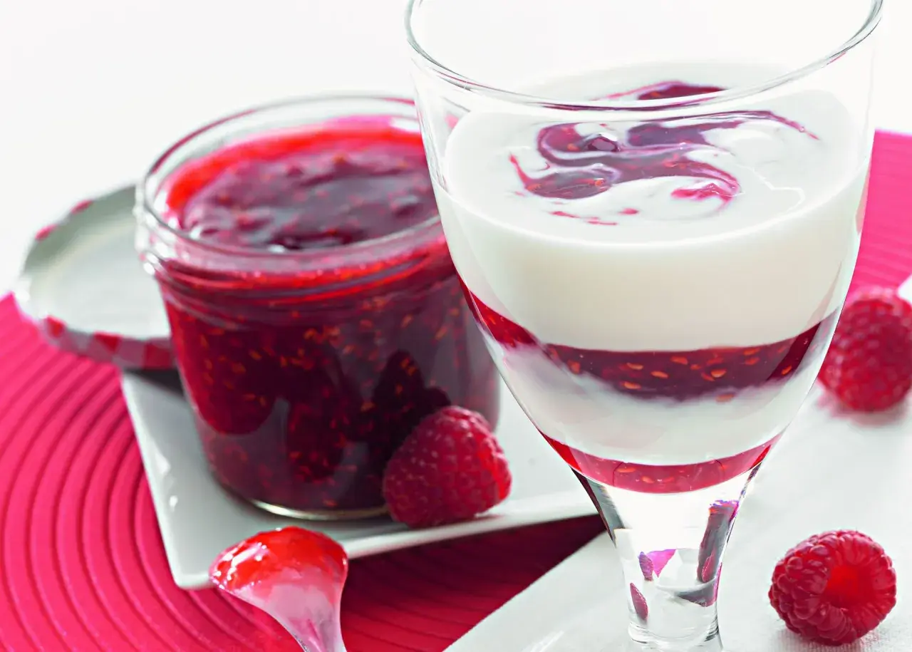 Sok z malin Thermomix w deserze jogurtowym. Słoiczek domowej konfitury malinowej obok.