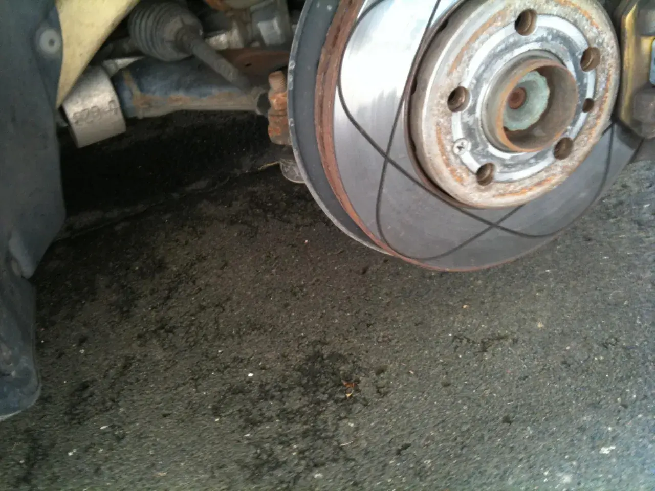 Nahaufnahme einer Bremsscheibe mit Rillen, die auf das Einbremsen der Bremsen hinweisen. Rostige Teile und eine schwarze Reifenflanke sind sichtbar.