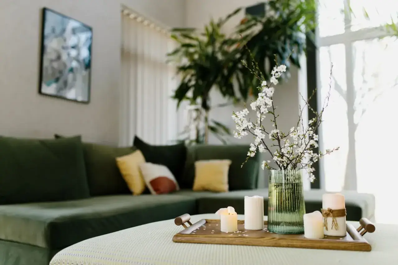 Stolik z świecami i gałązką kwitnącej wiśni, zielona kanapa w tle. Aranżacja zgodna z zasadami feng shui, wprowadzająca harmonię.
