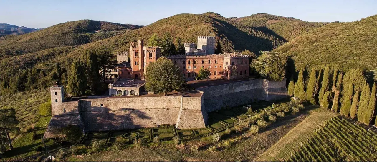 Il Castello di Brolio, imponente fortezza in mattoni rossi, domina le colline toscane, circondato da vigneti e cipressi.