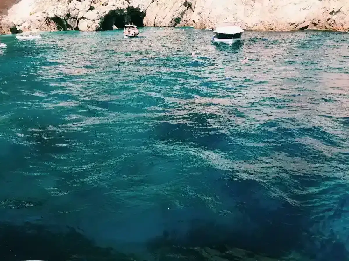Acqua cristallina e turchese vicino all'ingresso di una grotta, con barche e bagnanti che godono della bellezza della Grotta Azzurra.