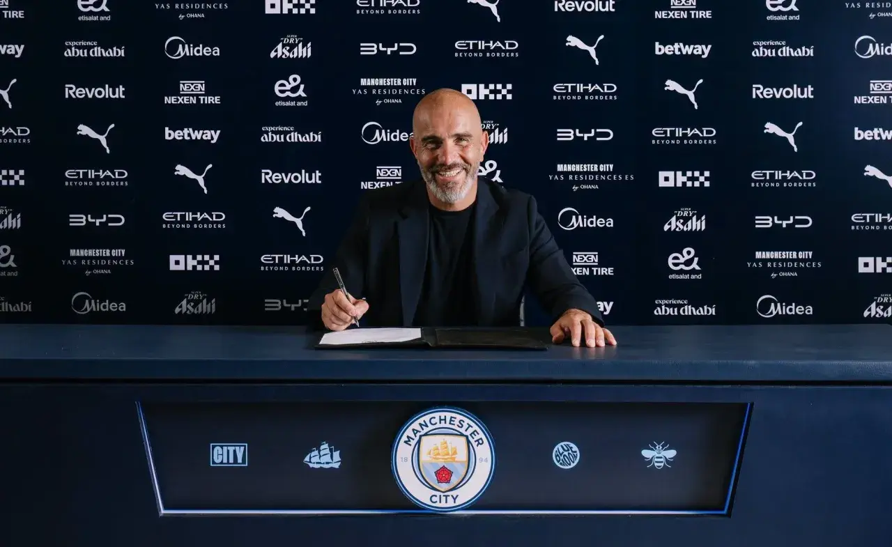 Uśmiechnięty trener Manchesteru City podpisuje kontrakt.