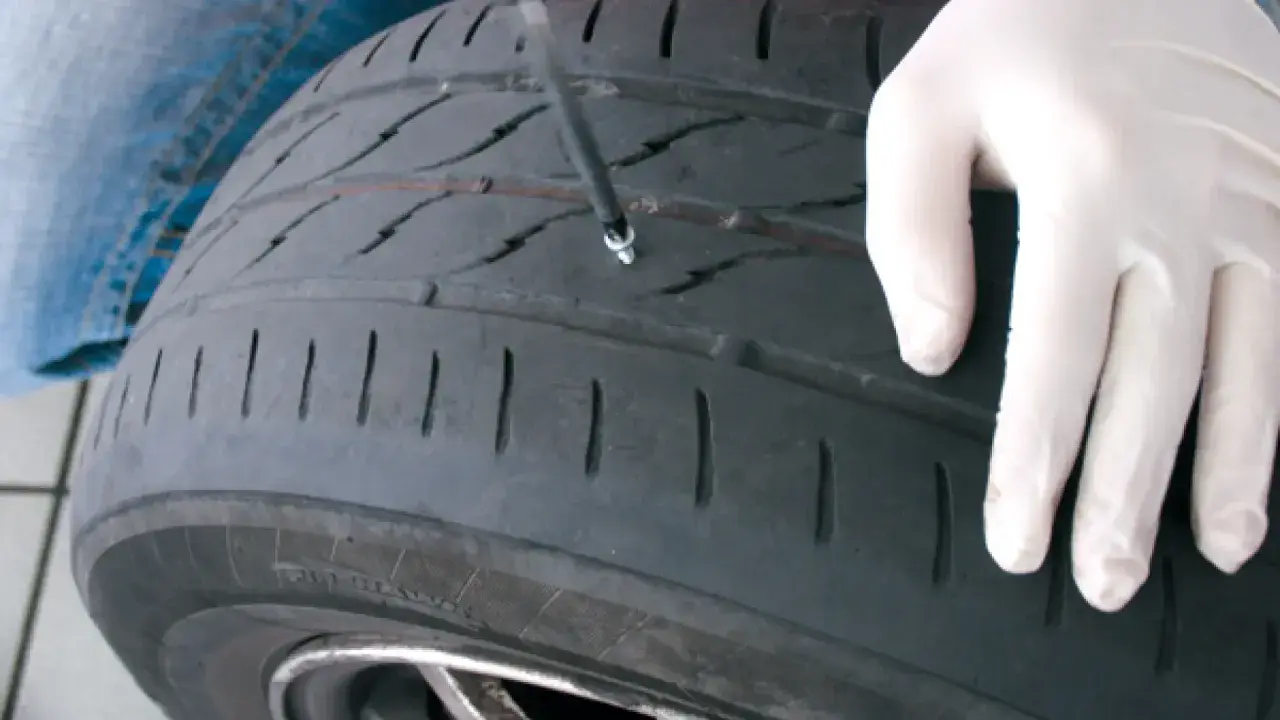 Mano enguantada inserta herramienta para reparar pinchazo. Es seguro reparar un pinchazo si se hace correctamente.