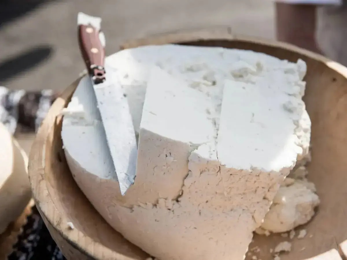 Formaggio fresco e morbido, simile a uno stracchino, tagliato in una ciotola di legno con un coltello.