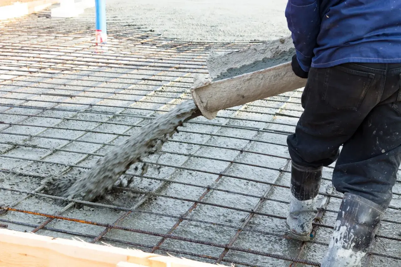 Betoniarz wylewa beton na zbrojenie, które zawiera włókna polipropylenowe, tworząc solidną posadzkę.