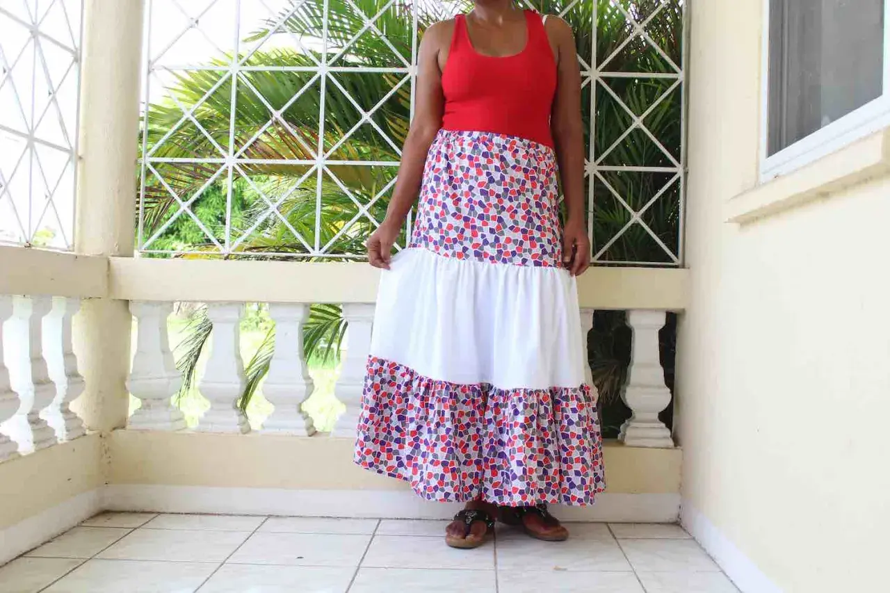 A woman models a long, tiered skirt with a colorful, mosaic-like pattern. The skirt features a white middle tier, creating a flowing, bohemian look.