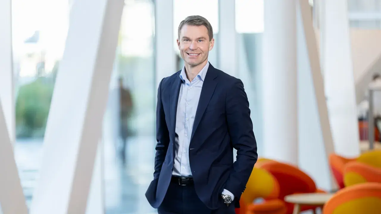 En leende man i mörkblå kostym, en del av Swedbank koncernledning, står framför ett modernt fönsterparti.