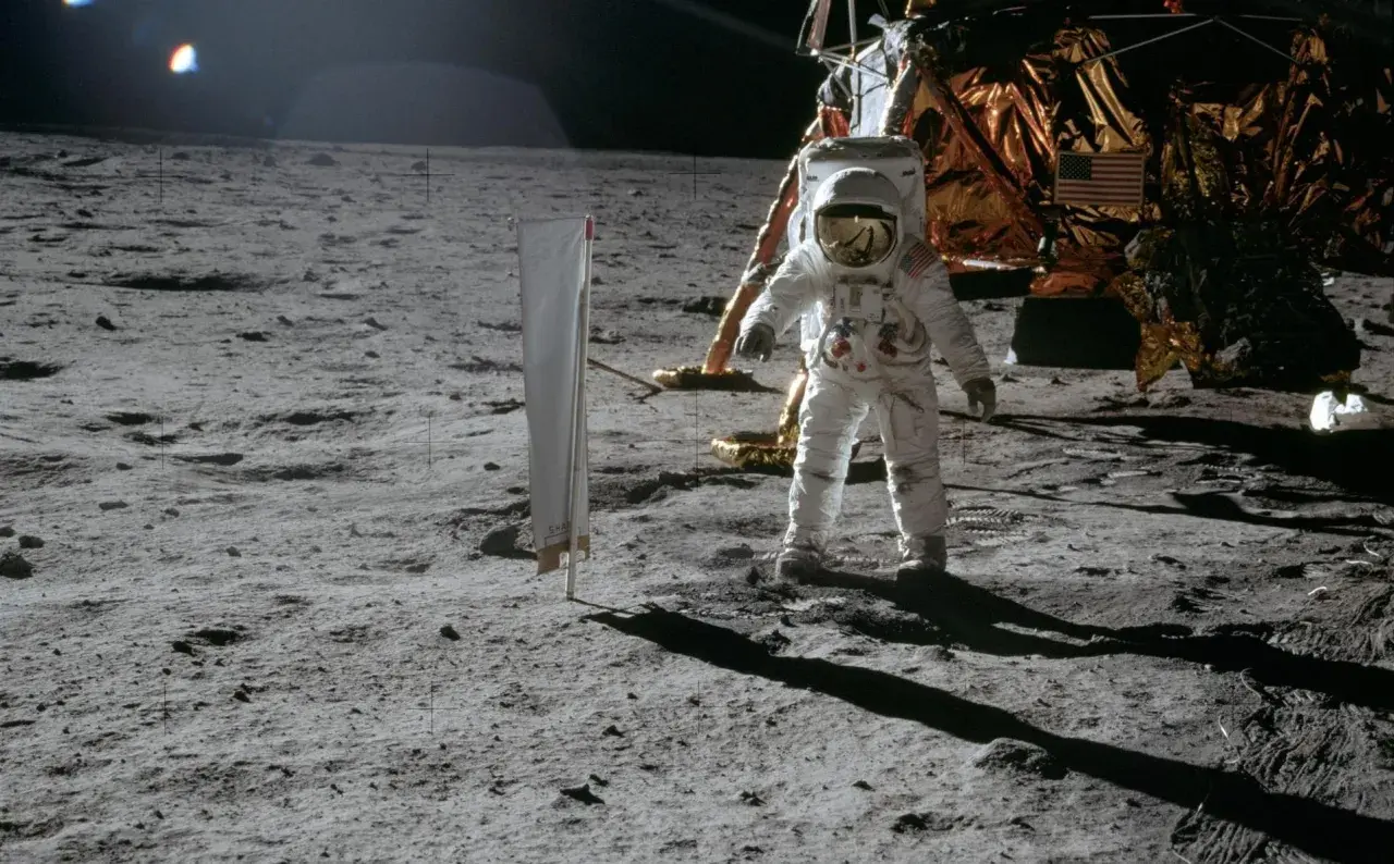 Astronaut na Księżycu podczas misji Apollo, obok lądownika. W tle amerykańska flaga.
