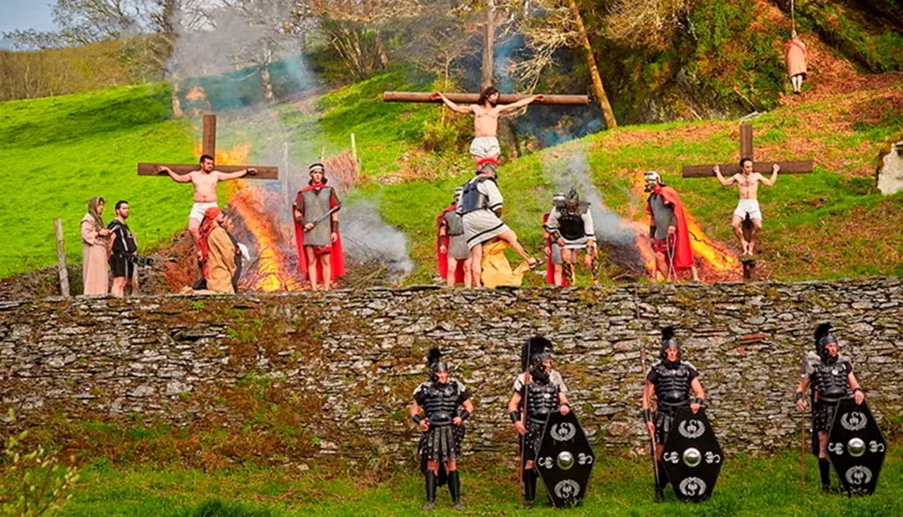 Recreación de la crucifixión en Semana Santa en Asturias. Hombres vestidos de romanos y figuras crucificadas en un paisaje verde.