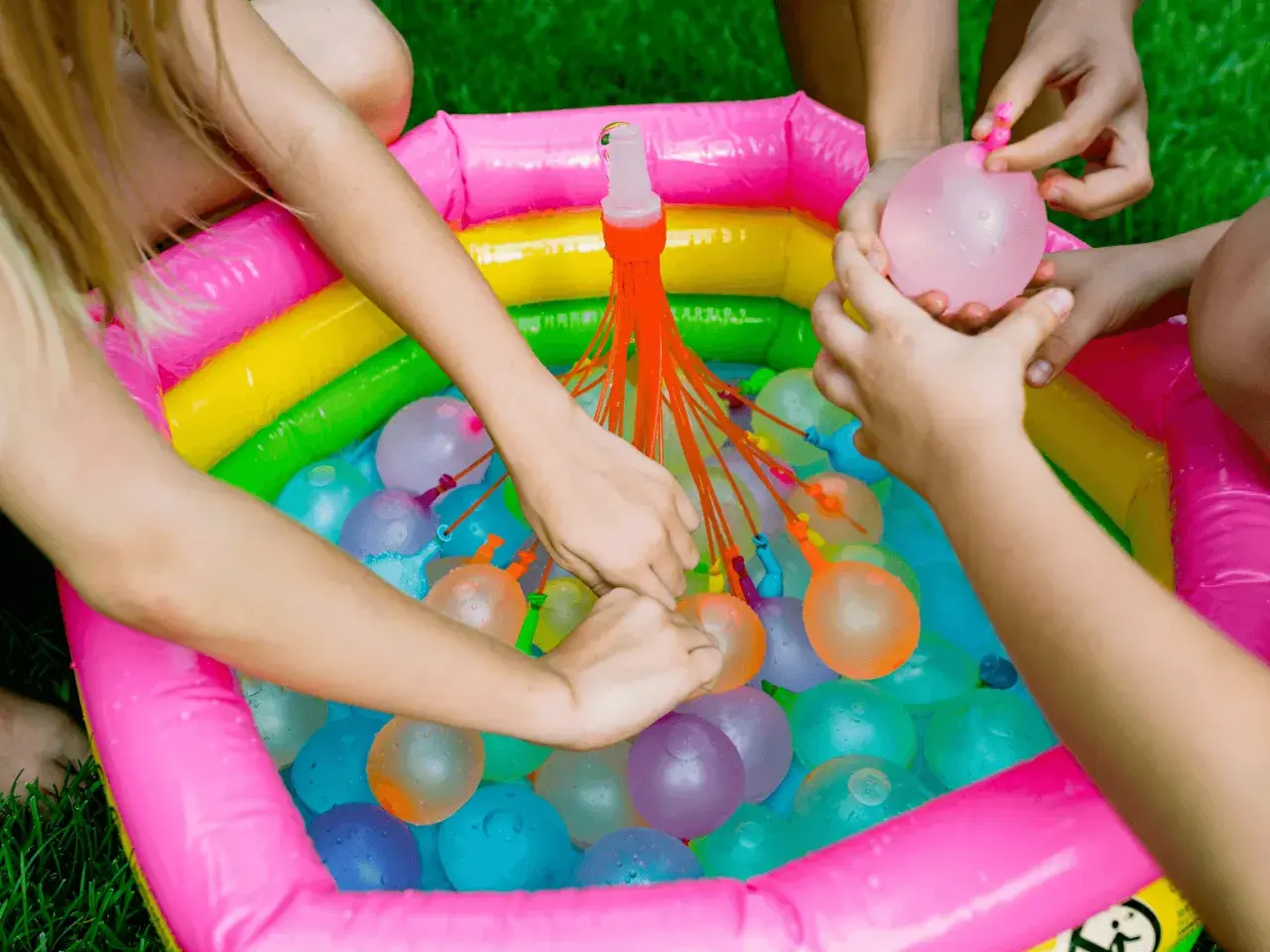 Manos infantiles llenando globos de agua en una piscina inflable multicolor. ¡Diversión garantizada con estos juegos de agua!
