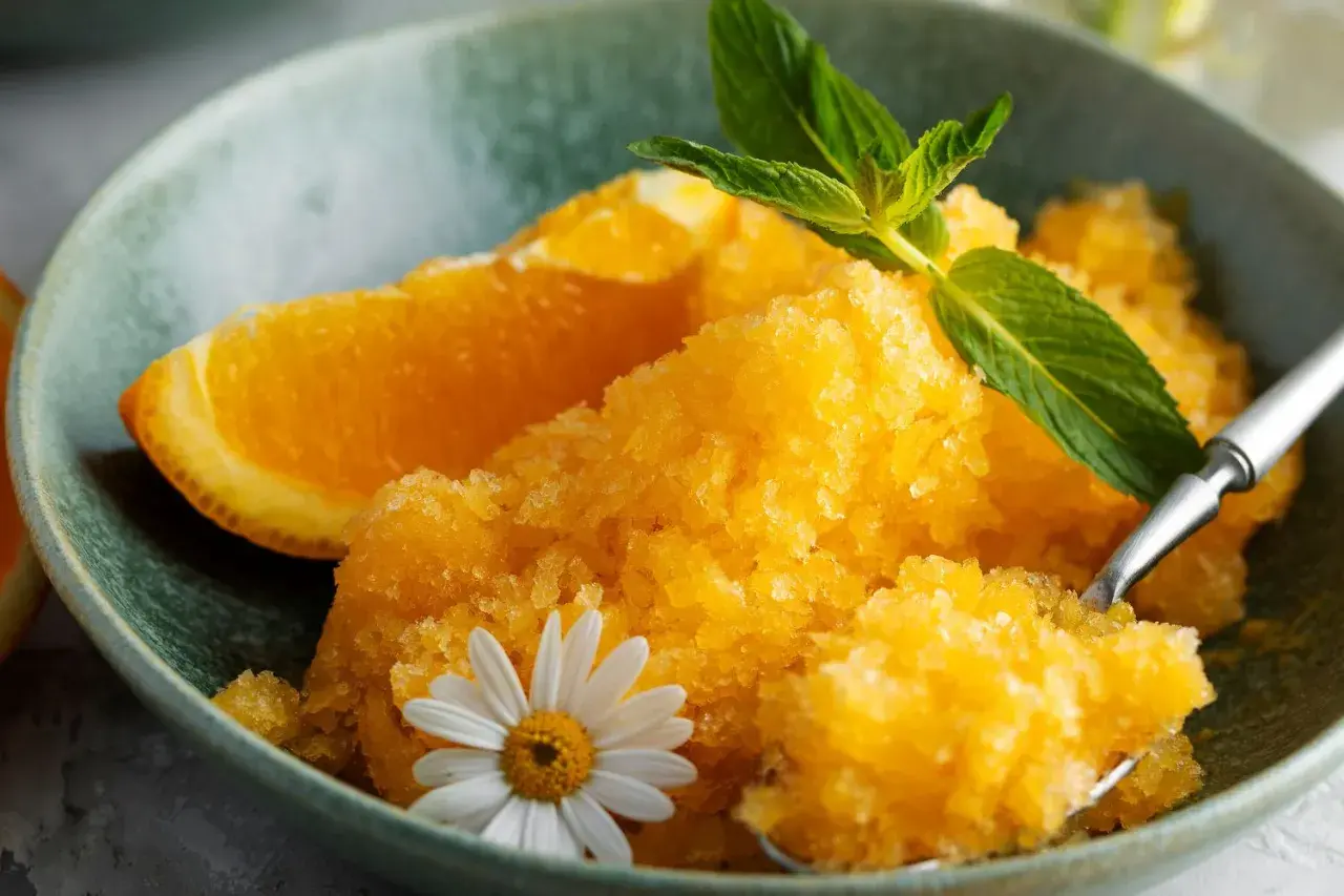 Pomarańczowy sorbet w misce z plasterkiem pomarańczy, miętą i kwiatkiem.