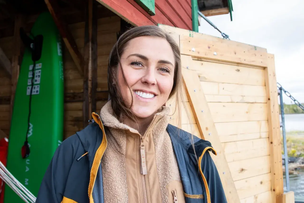 Amanda Robinson ler glatt framför en grön surfbräda och en träbyggnad.