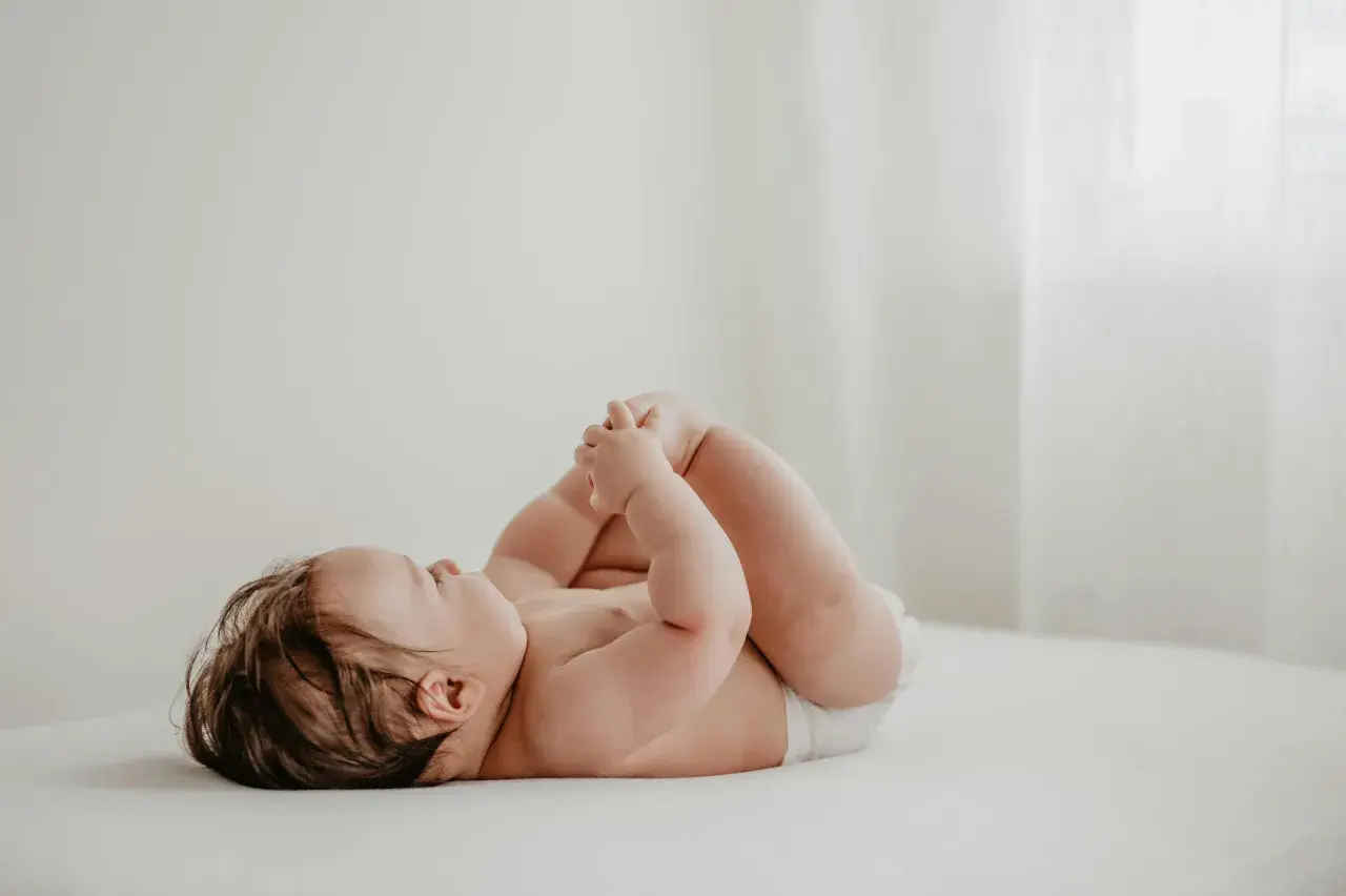 Un neonato con un adorabile culetto rosso, sdraiato su un lettino, gioca con i suoi piedini.