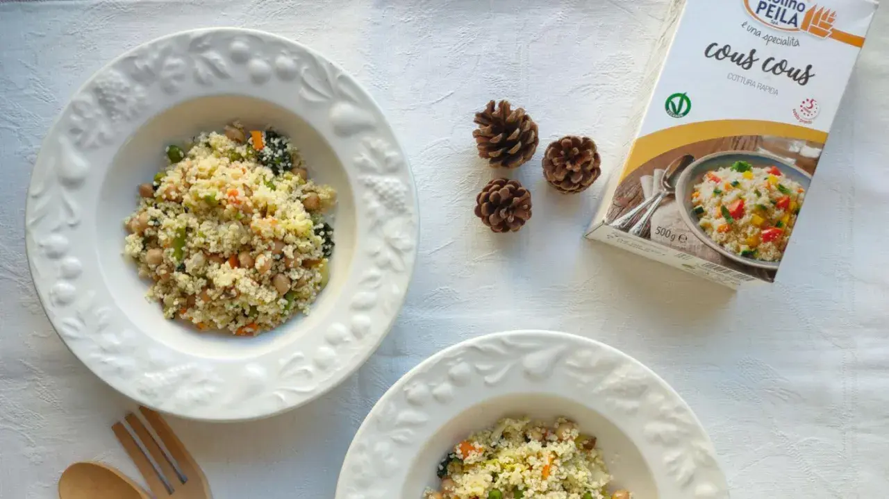 Piatti di cous cous con verdure e ceci, perfetti per le ricette cous cous invernale. Accanto, una confezione di cous cous e pigne decorative.