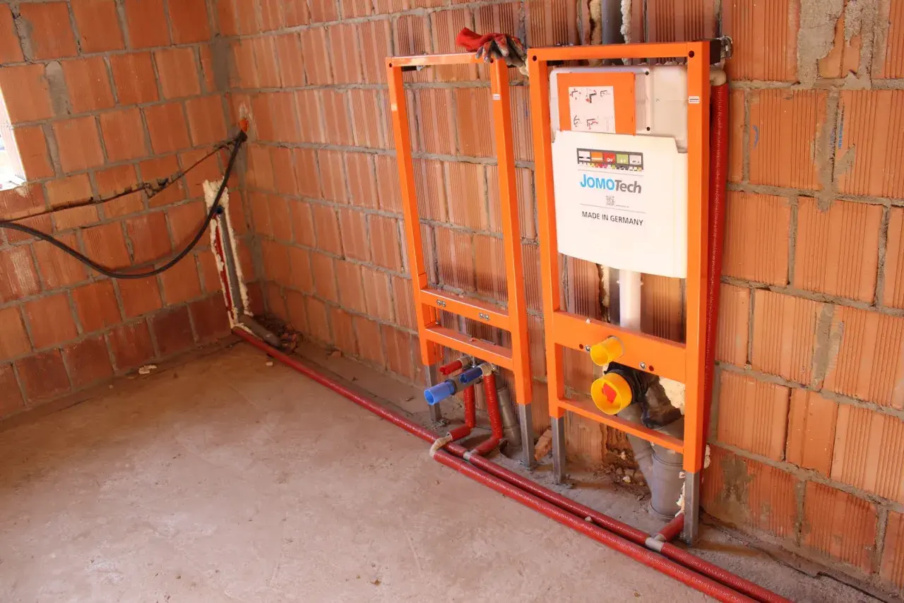Instalacja hydrauliczna przed tynkami: stelaże podtynkowe, rury i spłuczka JomoTech w budowie.