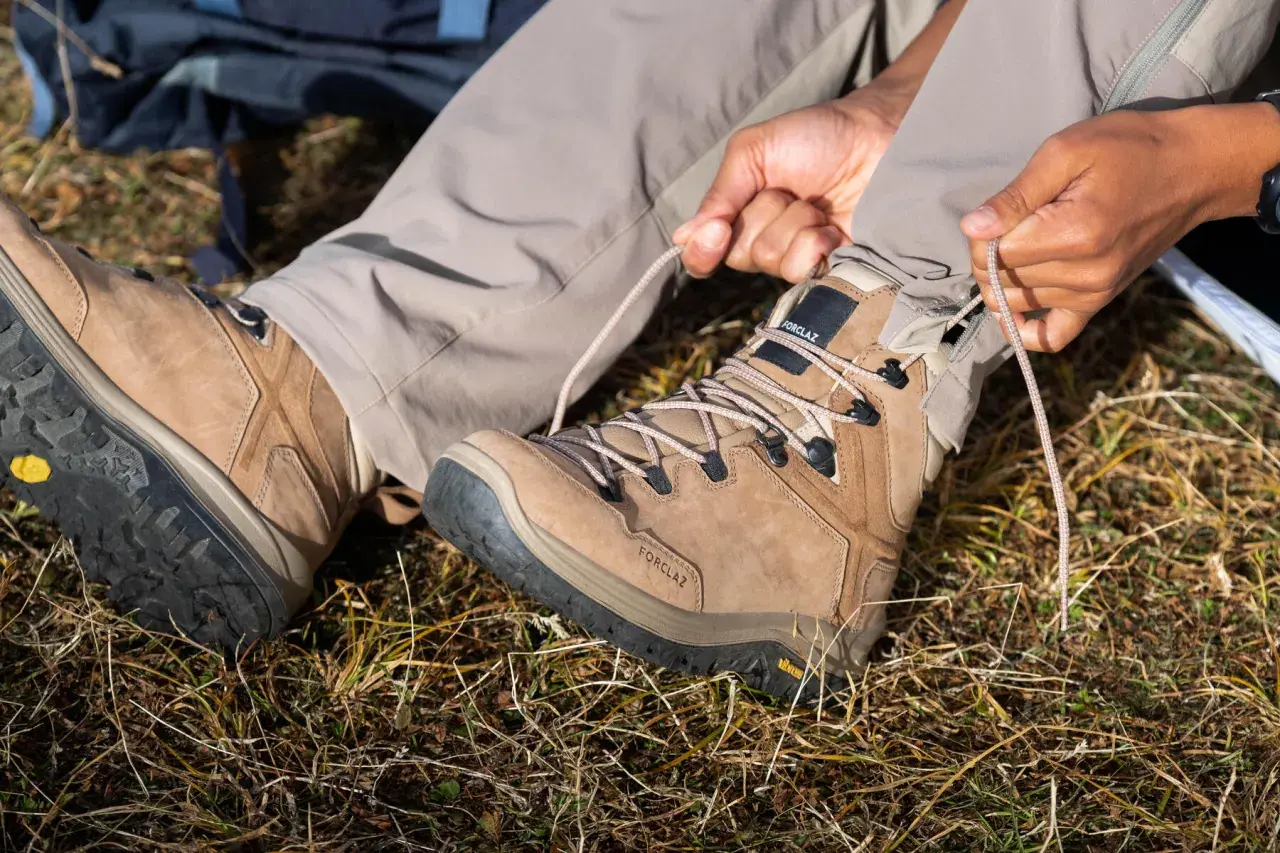 Ręce zaciskają sznurówki brązowego buta trekkingowego. Solidna podeszwa buta zapewnia przyczepność na nierównym terenie.