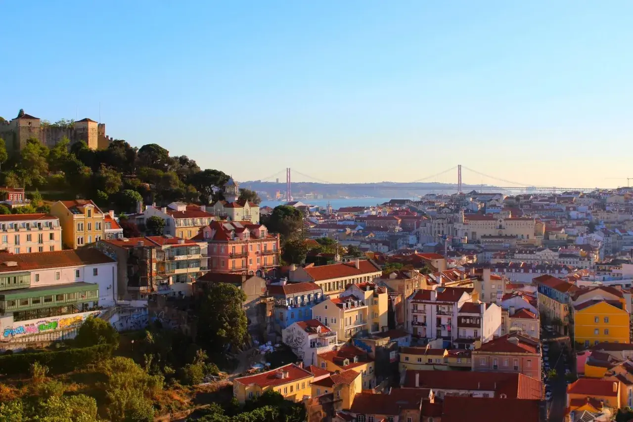 Vy över Lissabon med färgglada hus och en bro i fjärran. Perfekt för lissabon shopping och att uppleva stadens charm.