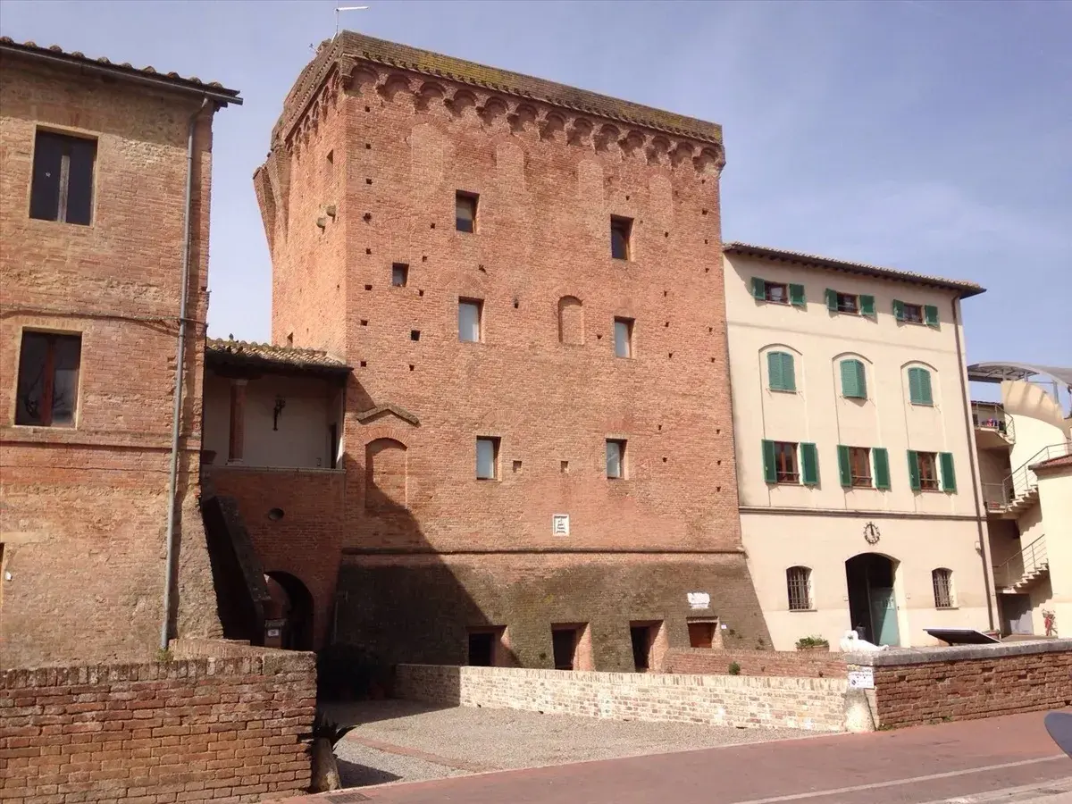 Torre medievale in mattoni a Monteroni d'Arbia, con edifici adiacenti in pietra e intonaco.