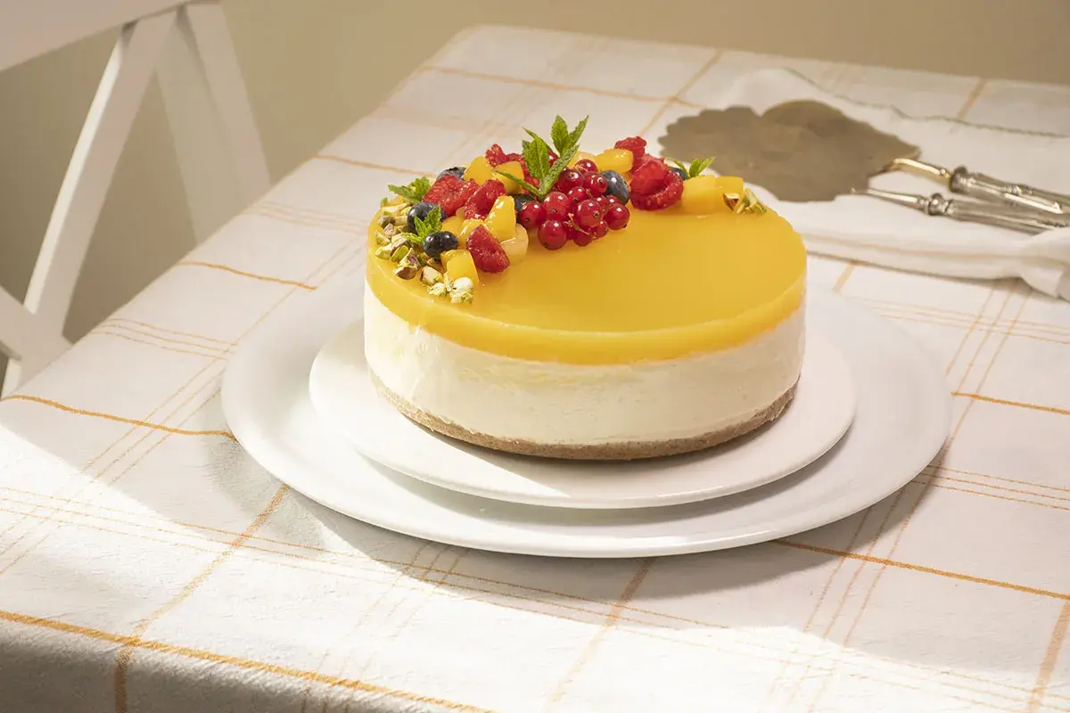 Deliciosa tarta de mango y queso, cubierta con gelatina amarilla y decorada con frutos rojos y pistachos.