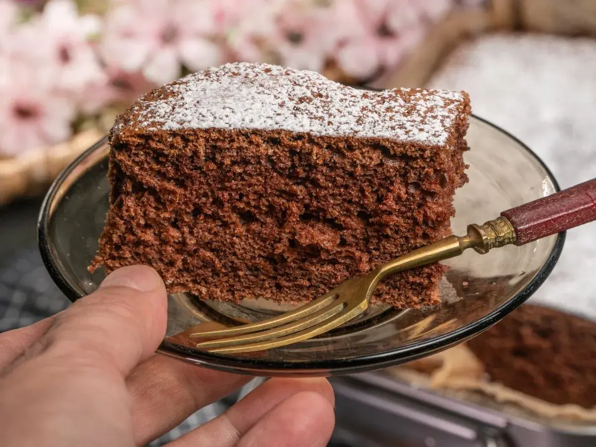 Kawałek najprostszego ciasta czekoladowego, posypana cukrem pudrem, na talerzyku z widelcem.